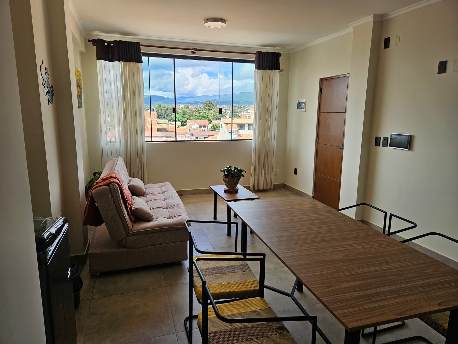 Living-comedor hacia la ventana, con vista a la ciudad y la serranía